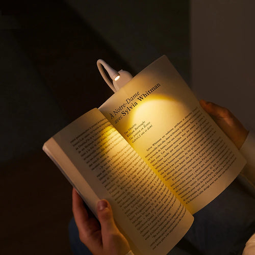 Mini book light clipped onto open book with warm LED glow in dark bedroom